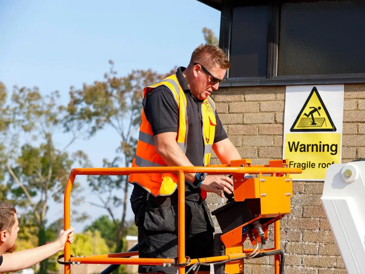 A Cornerstone Pest Control technician working from a boom lift beside a fragile roof warning sign
