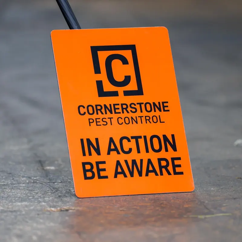 An orange Cornerstone Pest Control in action be aware warning board set out at a work site