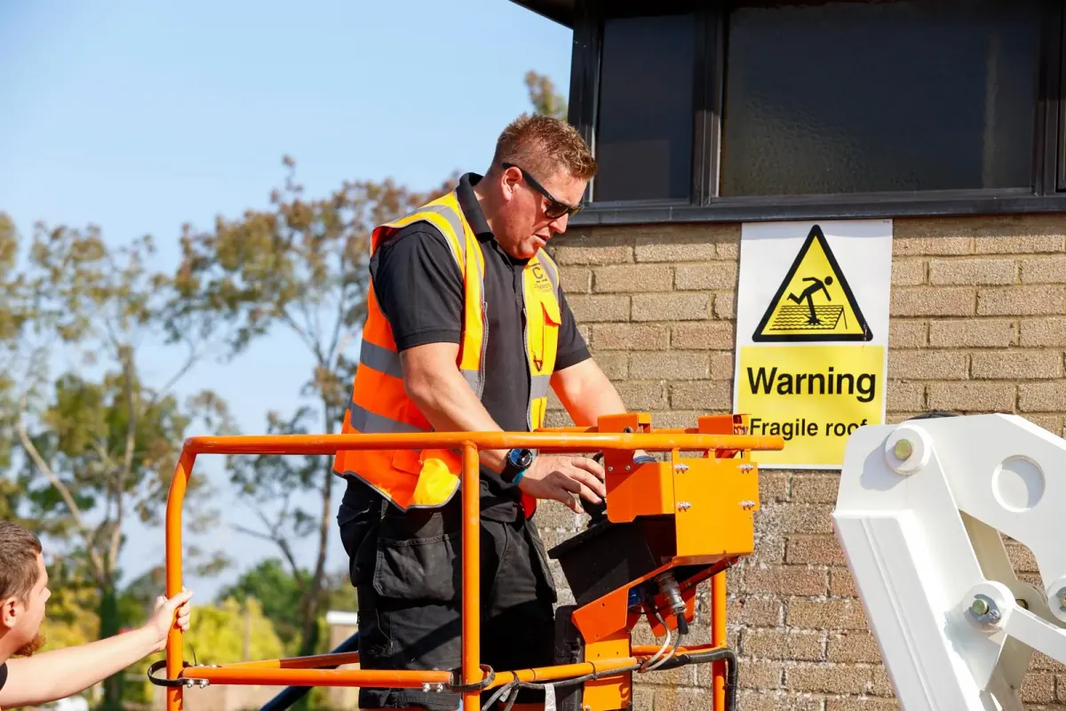 A Cornerstone Pest Control technician working from a boom lift next to a yellow fragile roof warning sign