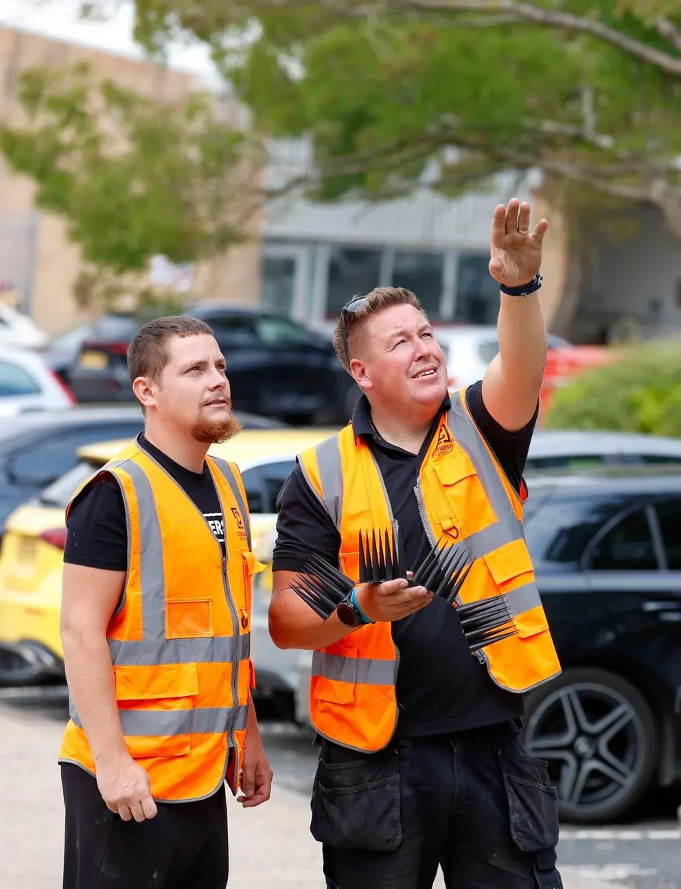 Two Cornerstone Pest Control technicians in hi-vis surveying the elevation of a building